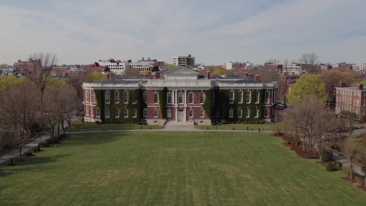 Aerial view of historic building surrounded by lush greenery and open lawn, showcasing architectural details and vibrant urban backdrop in a serene outdoor setting