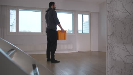 man walks through empty new house and picks up a box to unpack