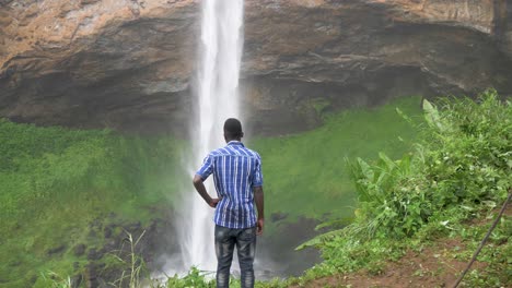 jóvenes africanos parados en la base de una gran y poderosa cascada en áfrica tropical