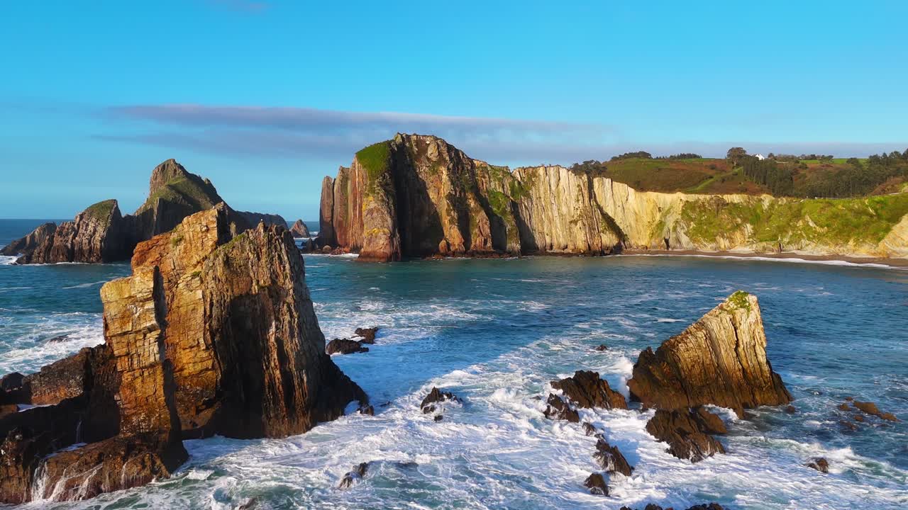 Ondas do oceano quebrando em torno de rochas com falésias ao fundo.