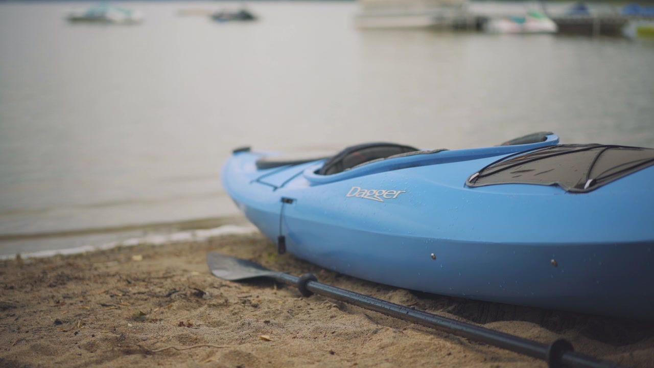 Kayak e pagaia su spiaggia sabbiosa con onde calme del lago che si infrangono in 4K ProRes