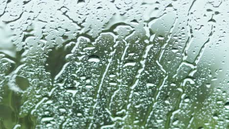 close-up view of raindrops trickling down a glass surface with a blurred green background.