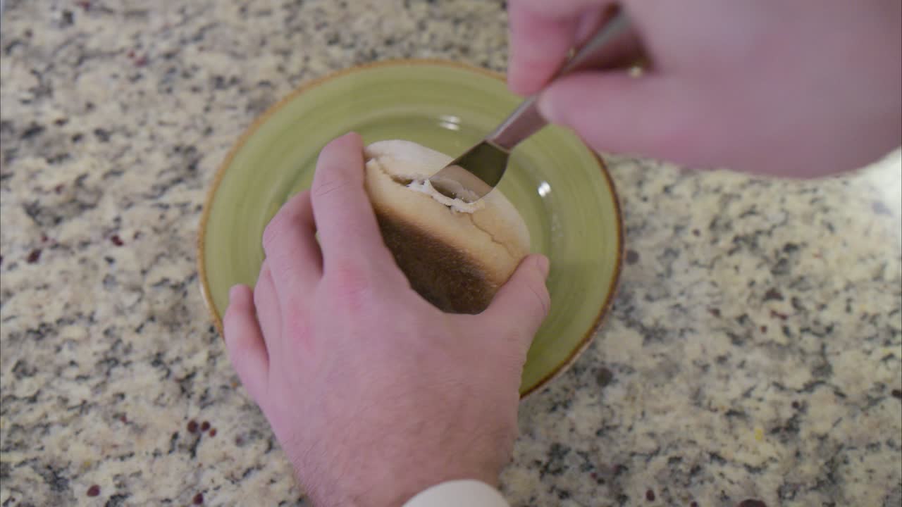 vista aérea de manos cortando un muffin inglés en dos para ser tostado para un desayuno saludable y nutritivo