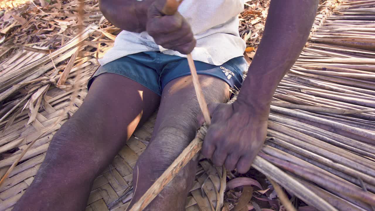 A native of Moheli or Mwali, Comoros making a wandza roof element on the ground - close up