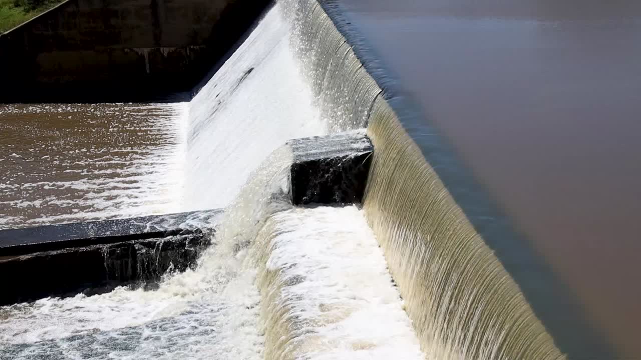 Close-up of a small dam's spillway with water surging over, capturing dynamic flow. Ideal for nature, hydrology, and environmental projects