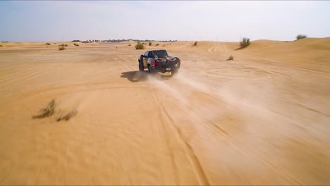 Black-4x4-truck-races-down-an-off-road-path-near-sand-dunes-in-the-desert-outside-of-Dubai,-UAE