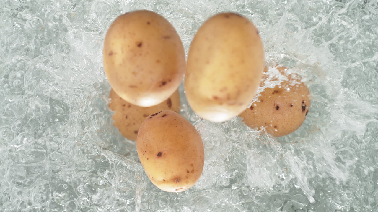 Patate con la buccia che cadono in una pentola di acqua bollente creando uno schizzo al rallentatore, vista dall'alto