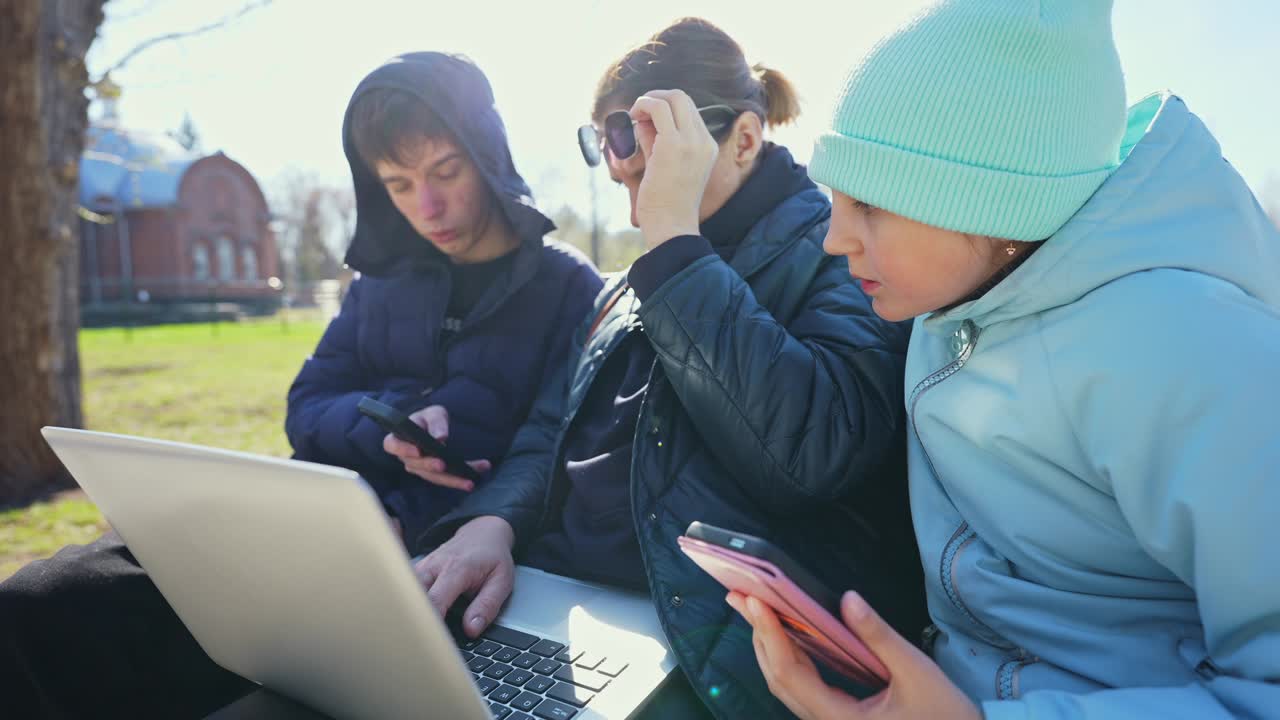公園のベンチでノートパソコンとスマートフォンを使う人々