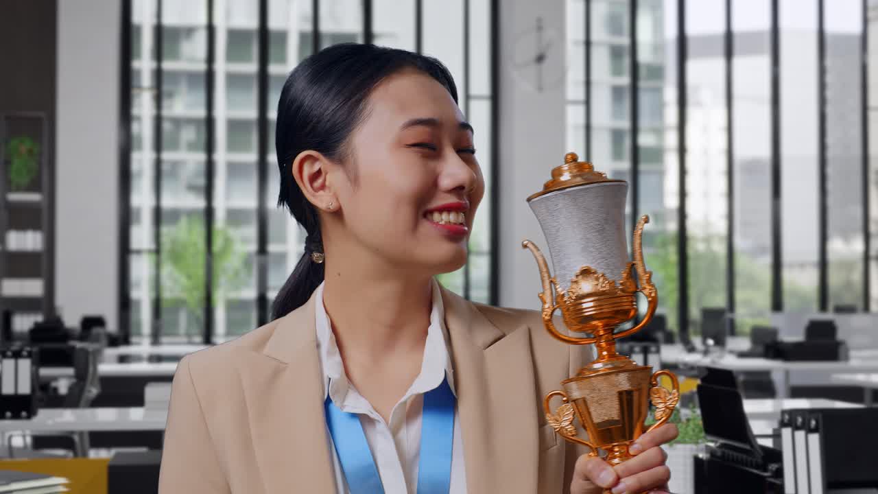 Close Up Of Asian Business Woman In A Suit With A Gold Medal Kissing A Gold Trophy Being Proud Winning As The First Winner In The Office