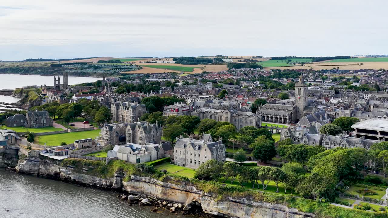 Drone glides above St Andrews coastline, revealing castle, cathedral ruins, university, and dramatic cliffs