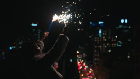 Fröhliche-Junge-Afroamerikanische-Frau-Mit-Wunderkerzen,-Die-Nachts-Auf-Dem-Dach-Tanzt-Und-Silvester-Feiert