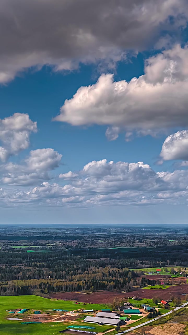 Clouds drift over rural farmland in a wide landscape timelapse, daytime scene