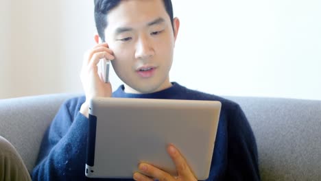 man talking on mobile phone while using digital tablet in living room 4k