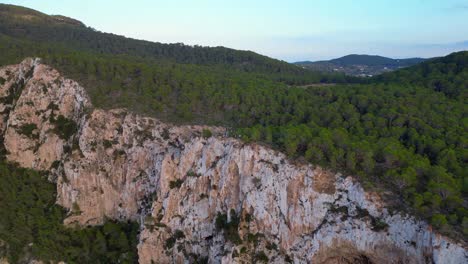 Hikers-rest-on-a-rocky-cliff-among-trees-with-a-view-of-the-green-landscape-during-sunset-in-ibiza