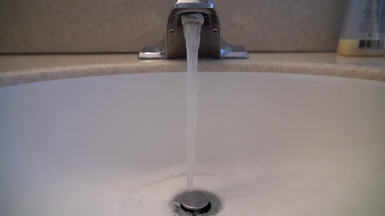 A close up shot of water running from a bathroom faucet into a basin set into a corian countertop.