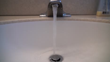 a close up shot of water running from a bathroom faucet into a basin set into a corian countertop.