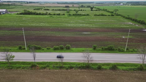 Vista-Panorámica-De-La-Carretera-Con-Coches-Que-Viajan-Cerca-De-Campos-Rurales