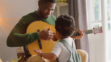 animation of light flashing over happy african american father and son playing guitar