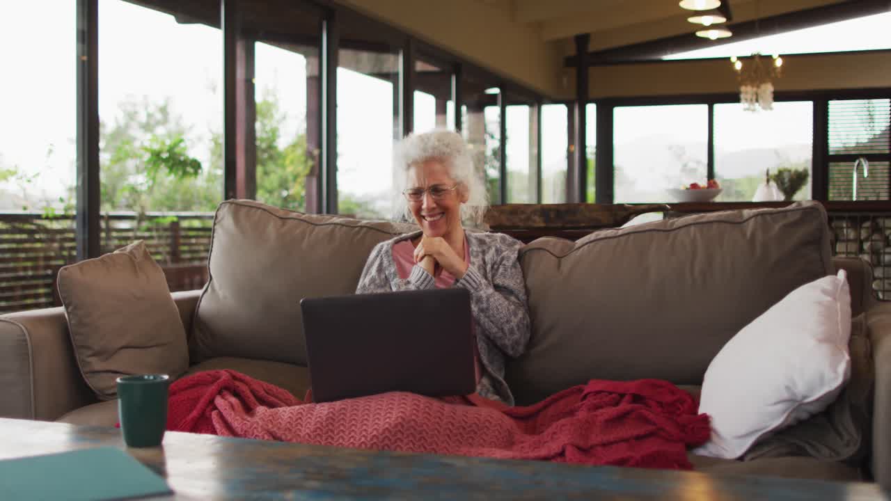 Senior mixed race woman sitting on sofa having video call using laptop