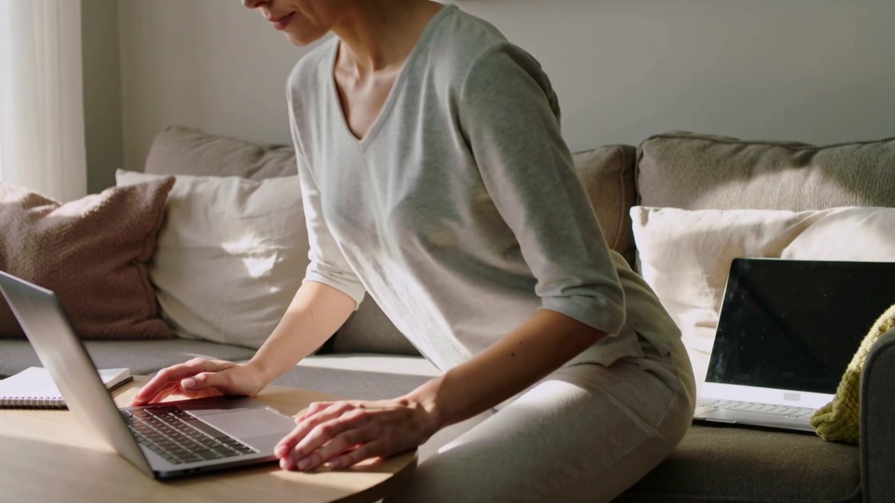 Leaning woman wearing light long-sleeve typing on laptop at coffee table, with pad and tablet