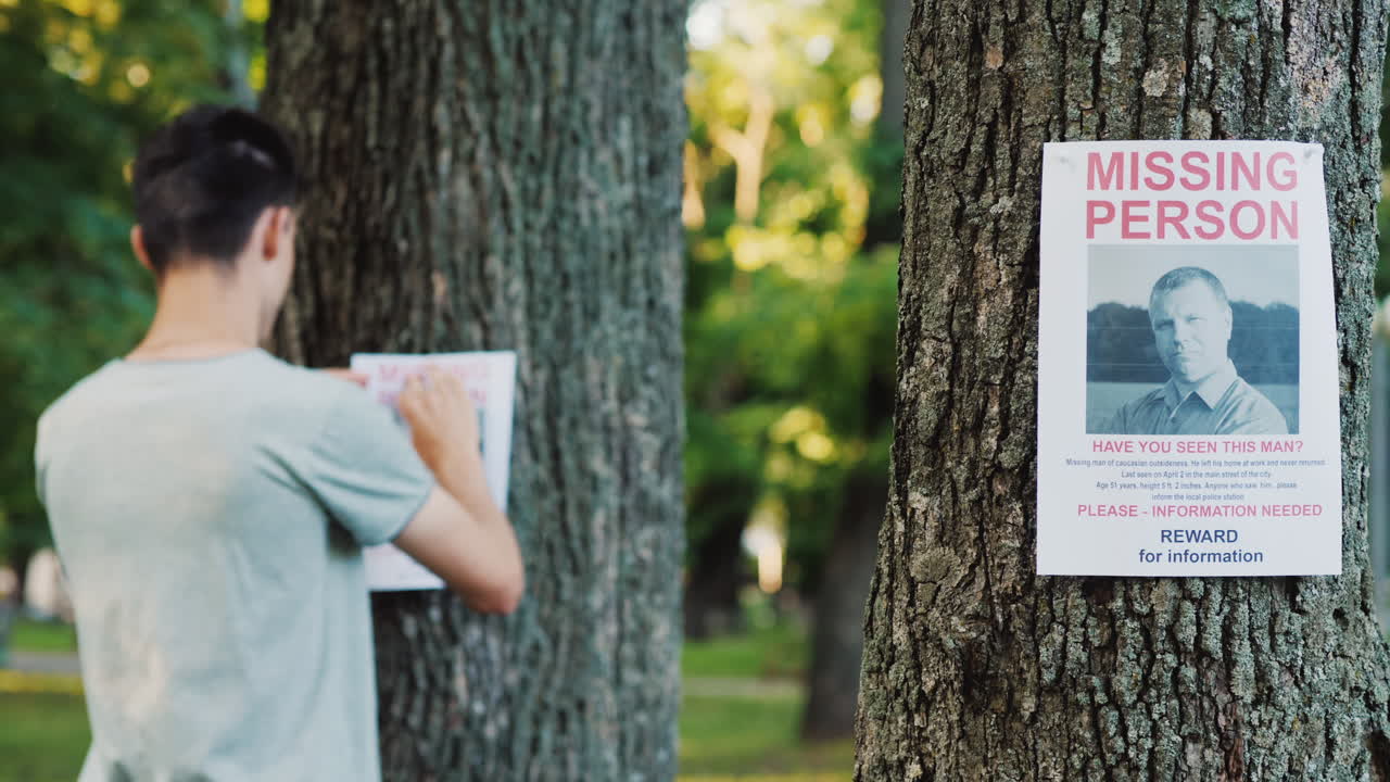 un joven pone anuncios de una persona desaparecida en el parque