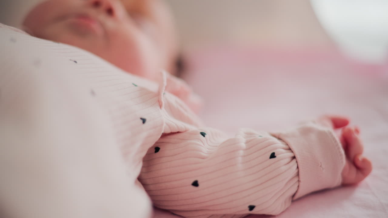 Bebè adorabile che riposa in un letto accogliente sotto la luce naturale, con indosso vestiti rosa pastello