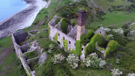 abandoned overgrown ivy covered desolate countryside historical welsh coastal brick factory mill aerial view descending to front shot