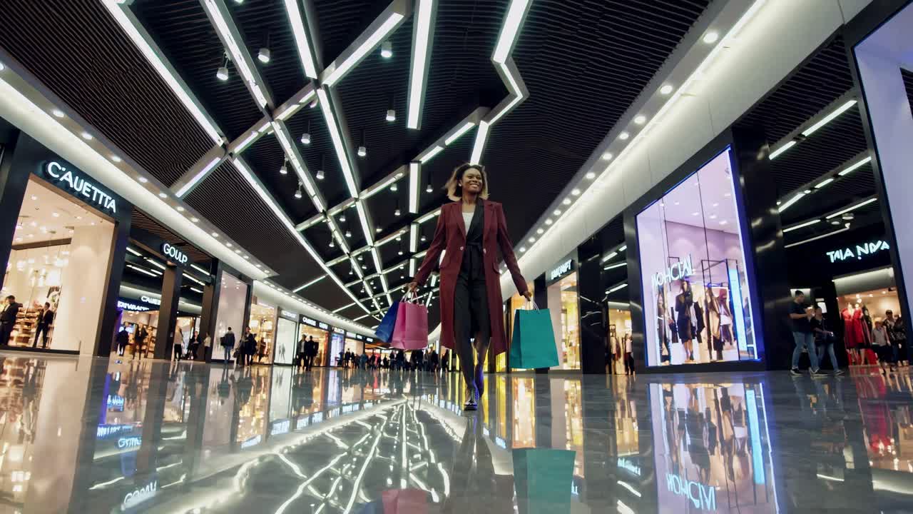 Low-angle shot of a stylish woman walking in a modern mall with shopping bags