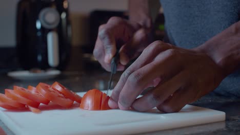 black man slicing fresh red tomatoes on plastic white cutting board in the kitchen