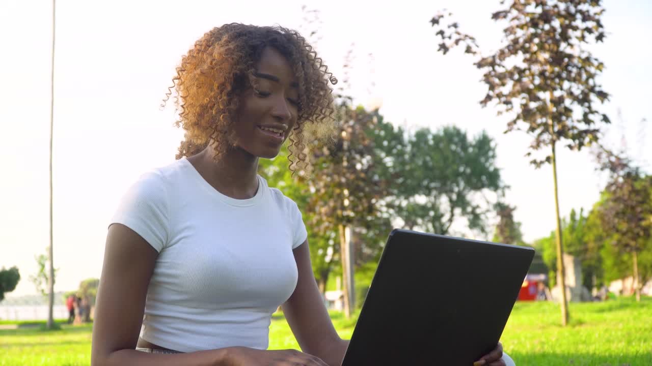 Smiling young african woman blogger influencer sit in park speaking looking at camera talking make video conference call record lifestyle blog concept