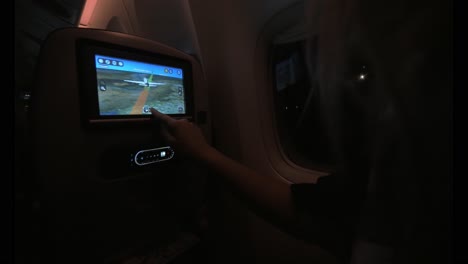 mujer usando el monitor del asiento en el avión por la noche