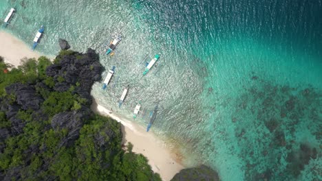 Aerial-top-down-spinning-view-of-beautiful-white-sand-secret-beach-with-huge-limestone-cliffs,-turquoise-water,-and-natural-archipelago-paradise-near-El-Nido,-Palawan,-Philippines