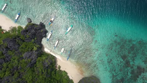 aerial top down spinning view of beautiful white sand secret beach with huge limestone cliffs, turquoise water, and natural archipelago paradise near el nido, palawan, philippines