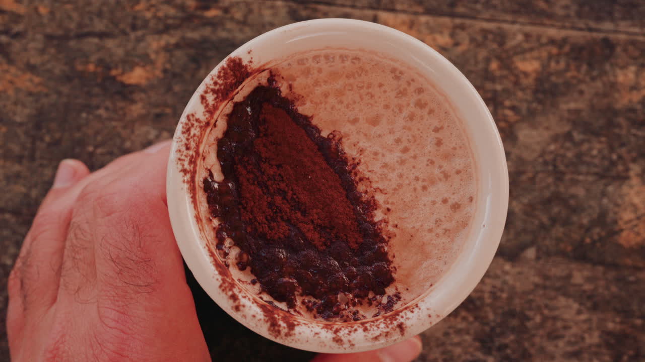 Woman's hand holding a cup of hot chocolate, with cocoa powder visible on top