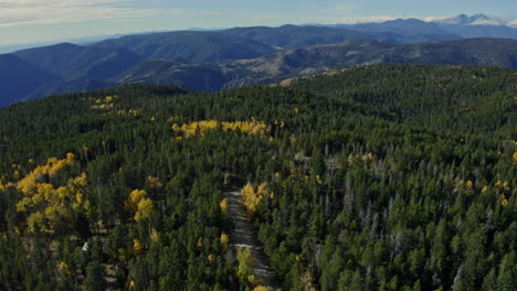 Orbiting-aerial-of-car-driving-through-yellow-aspens-in-fall-with-mountains,-4K