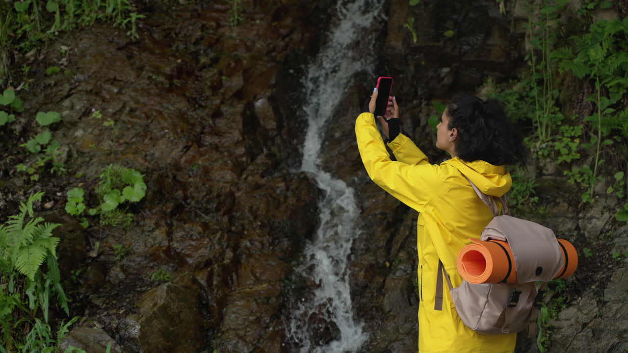 mujer tomando una foto de una cascada en la naturaleza