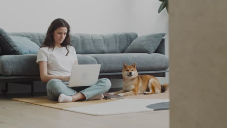 Schöne-Junge-Frau-Streichelt-Ihren-Süßen-Hund,-Während-Sie-Zu-Hause-An-Ihrem-Laptop-Arbeitet