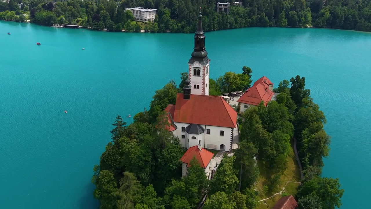 Isola di Bled, Slovenia. Ripresa drone di chiesa cattolica e torre in un boschetto verde circondate da acque alpine turchesi