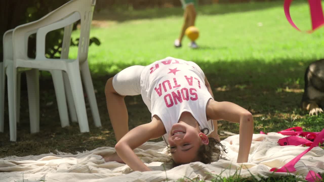niñas pequeñas en el campamento de verano jugando con cintas rosas haciendo gimnasia en el campo de hierba verde en cámara lenta