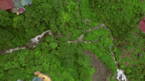 Aerial-of-green-forest-with-winding-stream-cutting-through-dense-foliage-in-Sapa,-Vietnam