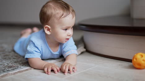 nice cute child lies on the floor watching the ball rolling in front of him. little boy crawling up to the toy watching it move. close up.