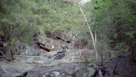 Ein-Bach,-Dessen-Wasser-In-Kaskaden-Die-Felsen-Hinunterfließt-Und-Zu-Einem-Wasserfall-Unter-Einer-Brücke-Fließt