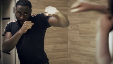 serious man practicing box in front of mirror at bathroom. portrait of black man