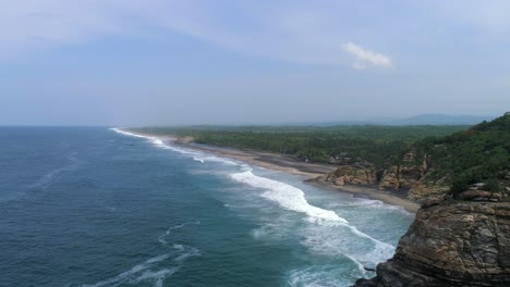 Aerial-pull-back-drone-shot-of-La-Ventanilla-with-rock-formations-and-waves,-Oaxaca