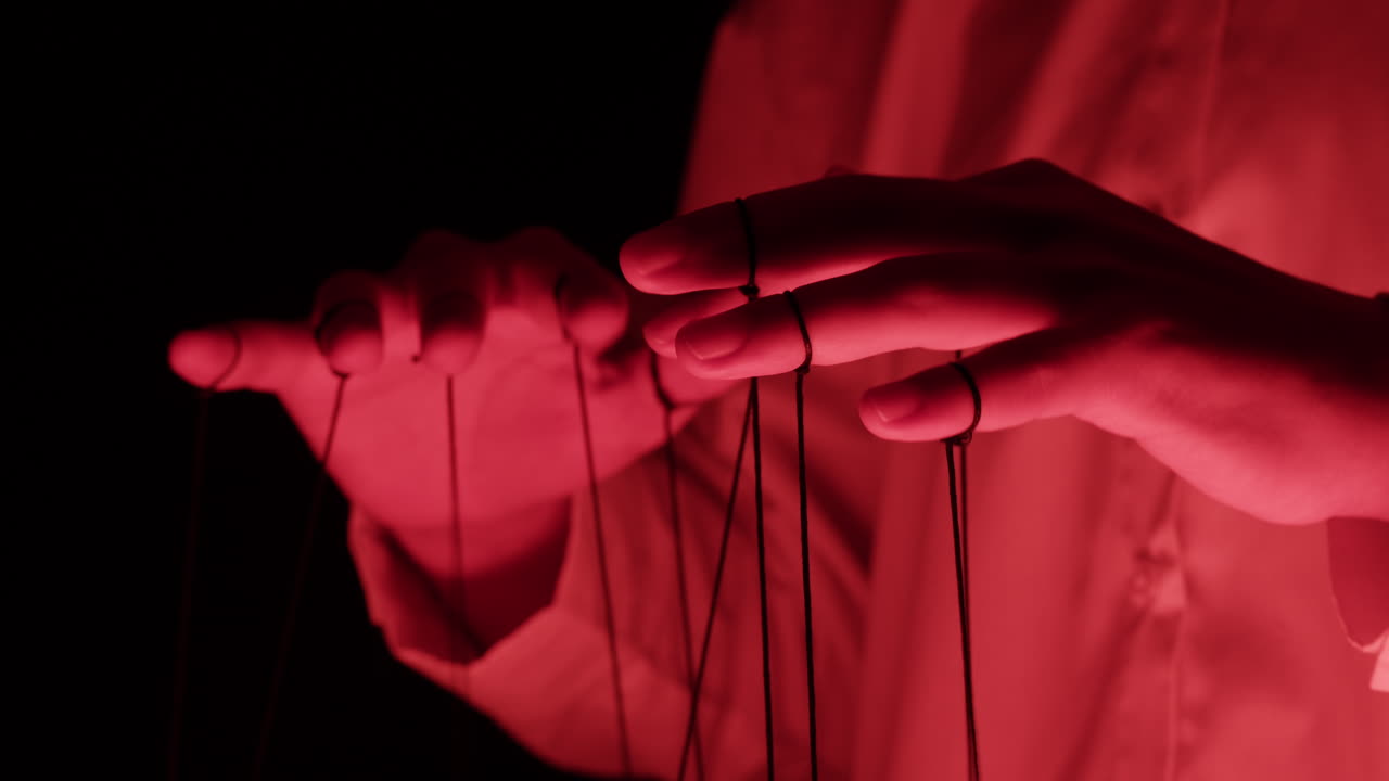 Human Hands Manipulating Puppet Strings Under Red Light
