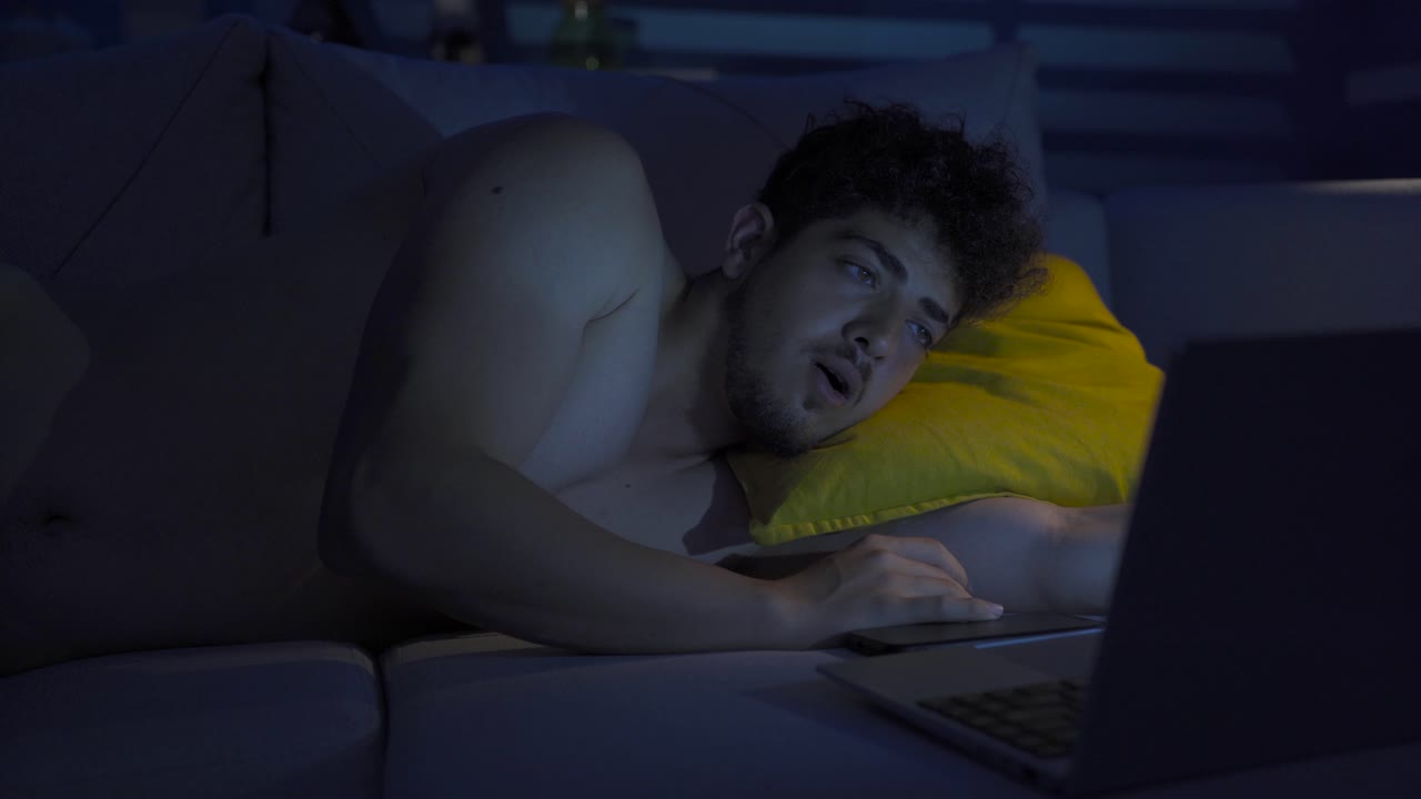un joven alegre mirando su computadora portátil tarde en la noche.