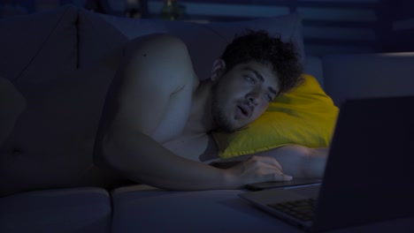 cheerful young man looking at laptop late at night.