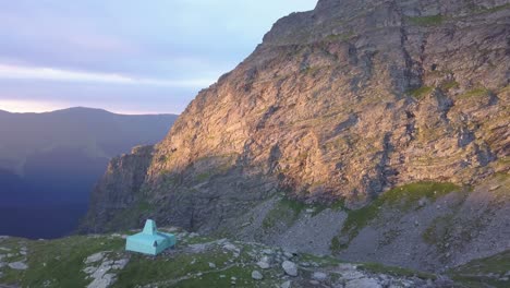 Wide-aerial-view-from-drone-circling-over-base-camp-on-small-plateau-with-rugged-terrain-and-steep-mountains-lit-with-golden-light-of-setting-sun