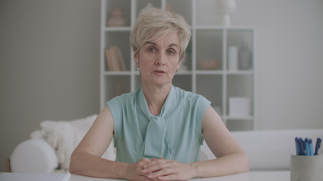 집에서 찍은 인터넷 초상화로 노인 여성의 비디오 전화 테이블에 앉아 카메라와 이야기하고 있습니다.