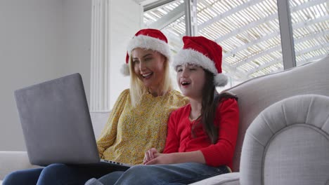 Mutter-Und-Tochter-Mit-Weihnachtsmütze-Unterhalten-Sich-Zu-Hause-Auf-Dem-Laptop-Per-Video